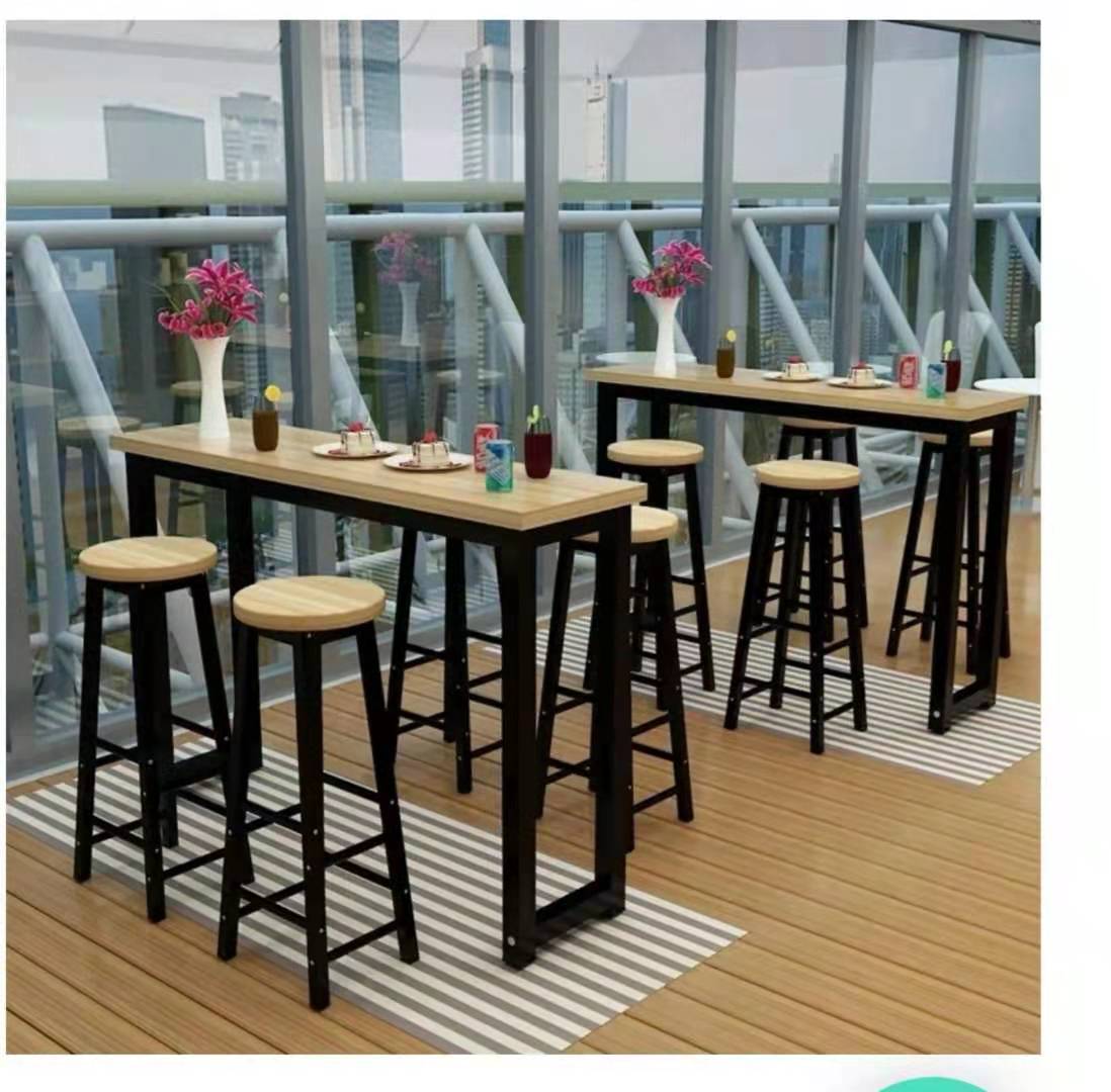 A bar table with a wood top and black frame, accompanied by stools, set against a backdrop of a glass-walled room with an urban landscape outside.